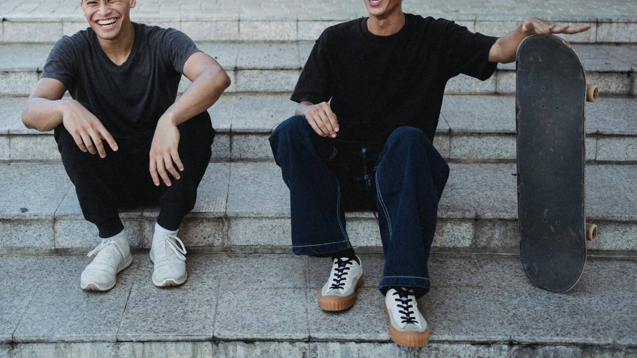 crop cheerful asian male friends resting on street steps